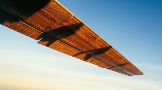 Vue panoramique d'une aile d'avion moderne en composite révélant sa structure interne avec effets de transparence montrant les fibres de carbone et nanoparticules